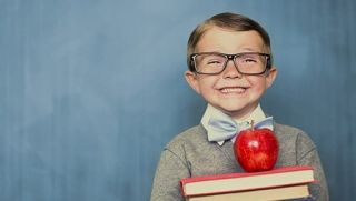 Happy child with glasses holding books and an apple on top